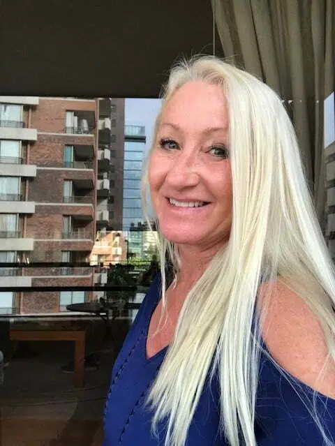 A woman with long white hair standing in front of a window.