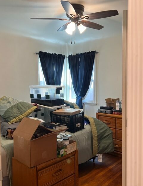 A room with many items on the bed and a fan