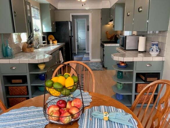 A kitchen with a table and chairs, and a bowl of fruit on the counter.