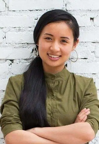 A woman with long black hair standing in front of a brick wall.